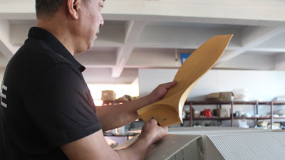 Quality control inspector checking the surface finish of solid wood ceiling fan blades at VANYE factory.